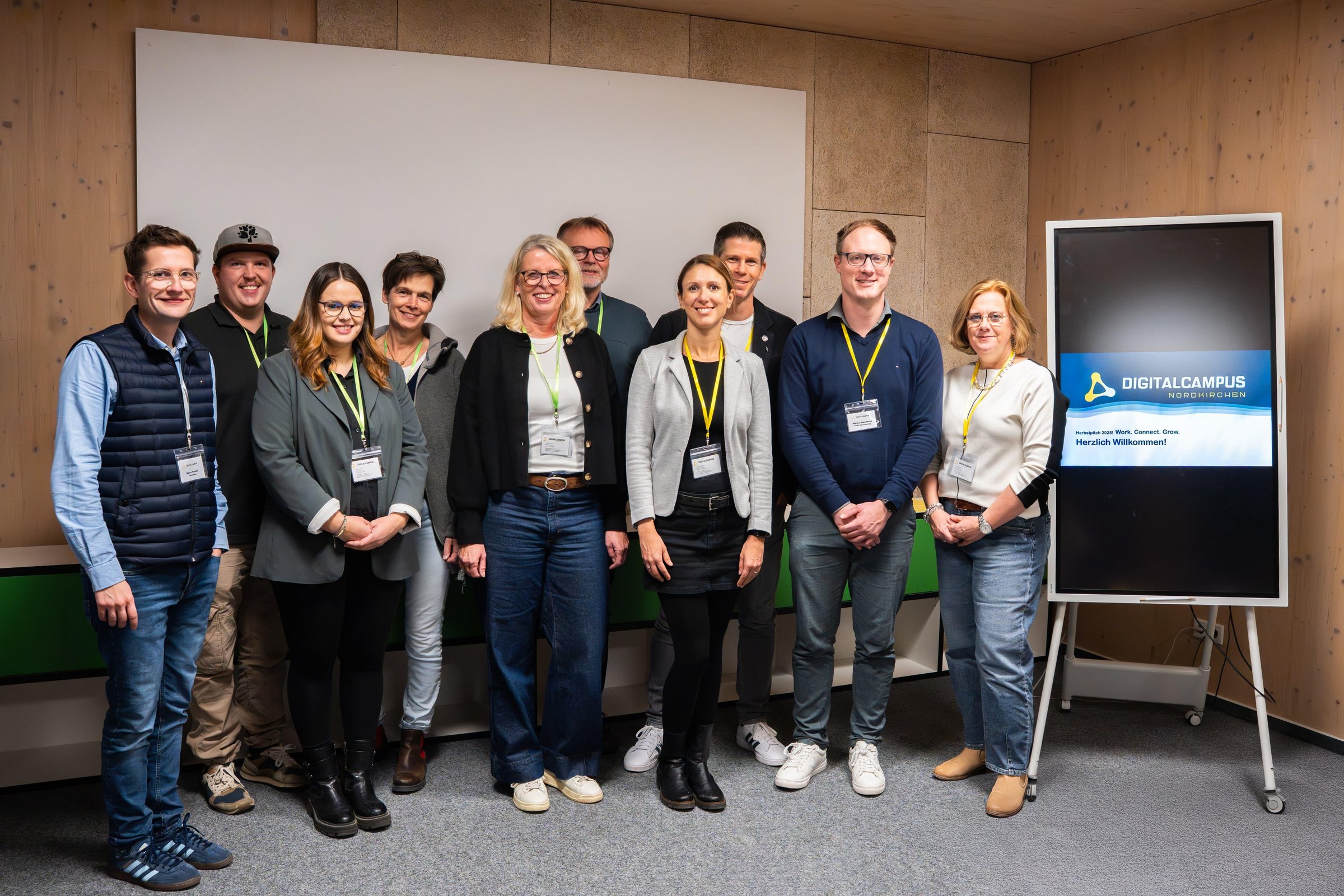Zehn Personen stehen in einer Gruppe zusammen. Neben ihnen ist ein Digitaldisplay auf dem das Logo und der Schriftzug des Digital Campus zu sehen sind.